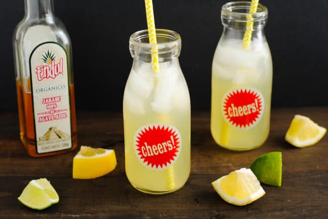 Bottle of agave nectar, and two glass bottles filled with lemonade and yellow straws.