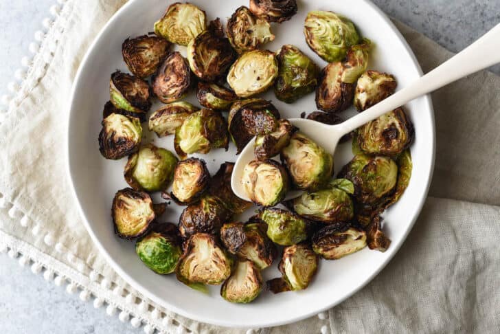 Air fried brussel sprouts in a white bowl with a white spoon.