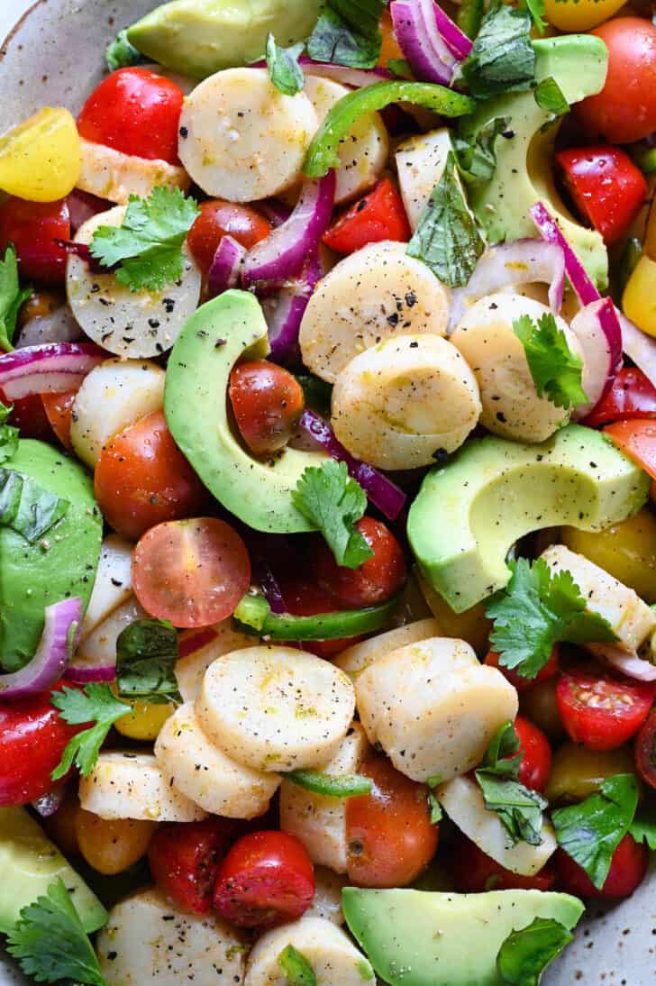 A closeup on a hearts of palm salad recipe with tomatoes and avocado.