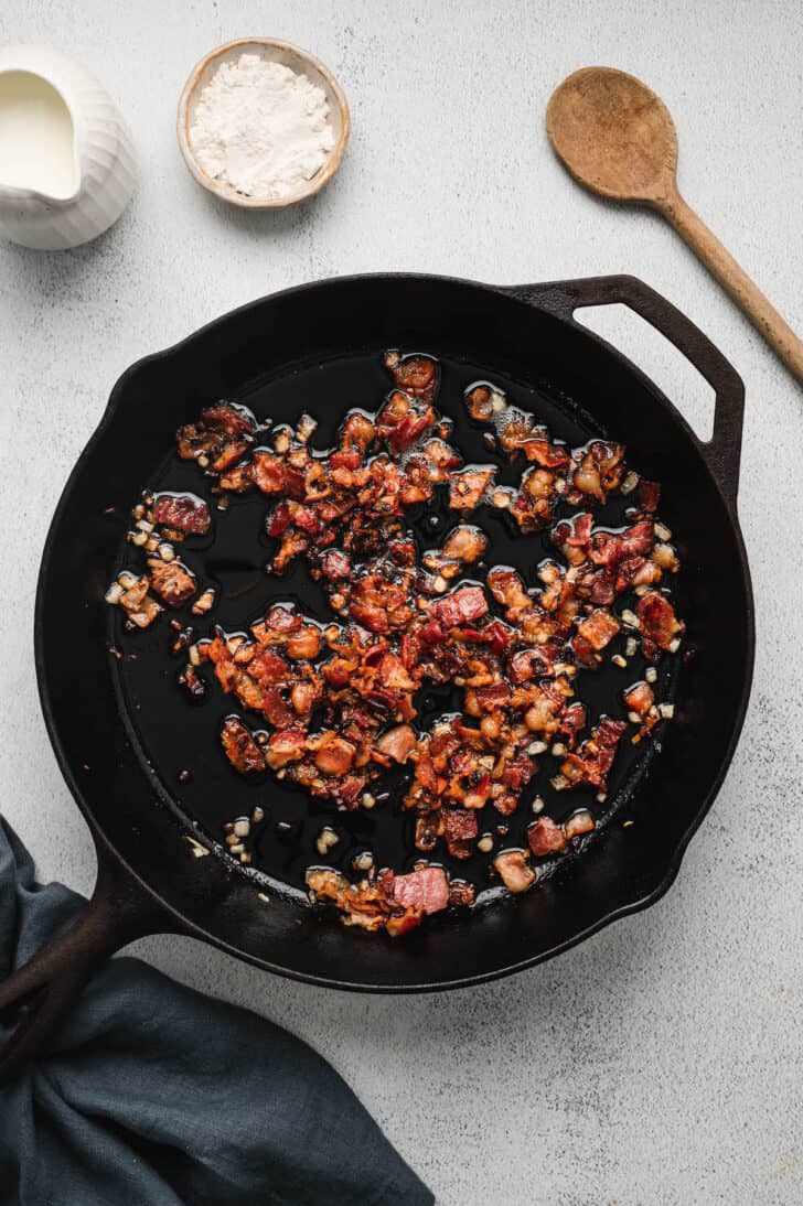 Chopped bacon frying in a cast iron skillet.