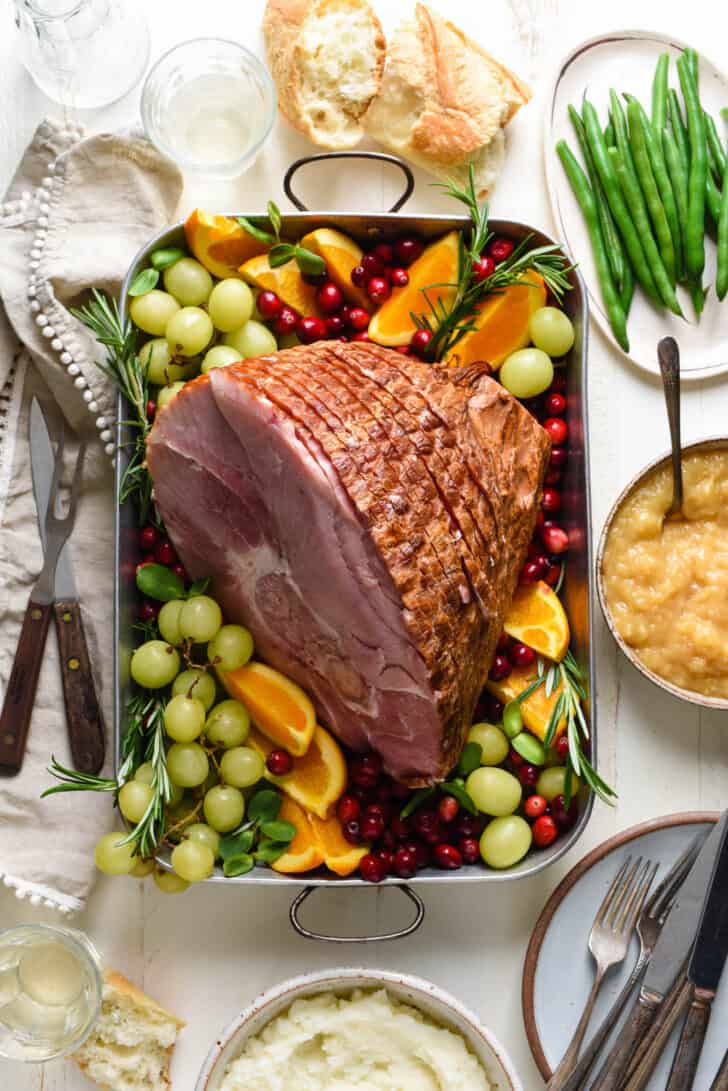 Holiday dinner scene with roasting pan of spiral sliced ham as centerpiece, with side dishes nearby.