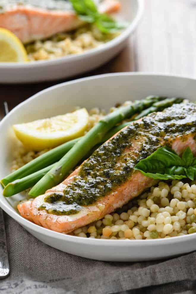 White plate filled with roasted fish with basil sauce, couscous and asparagus.