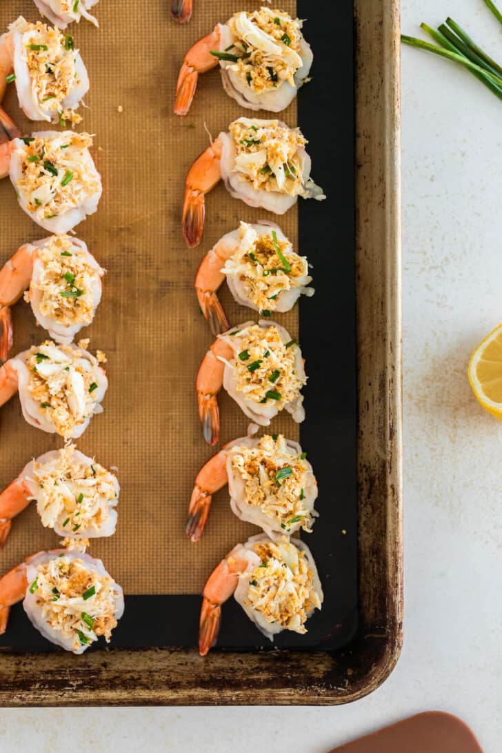 Butterflied prawns filled with a crab meat mixture on a baking pan.
