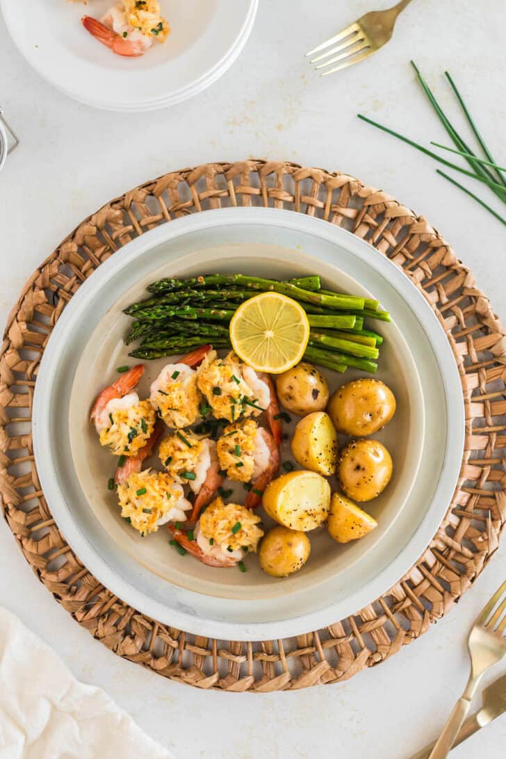 Crab stuffed shrimp, small yellow potatoes, asparagus, and a lemon half on a white plate.