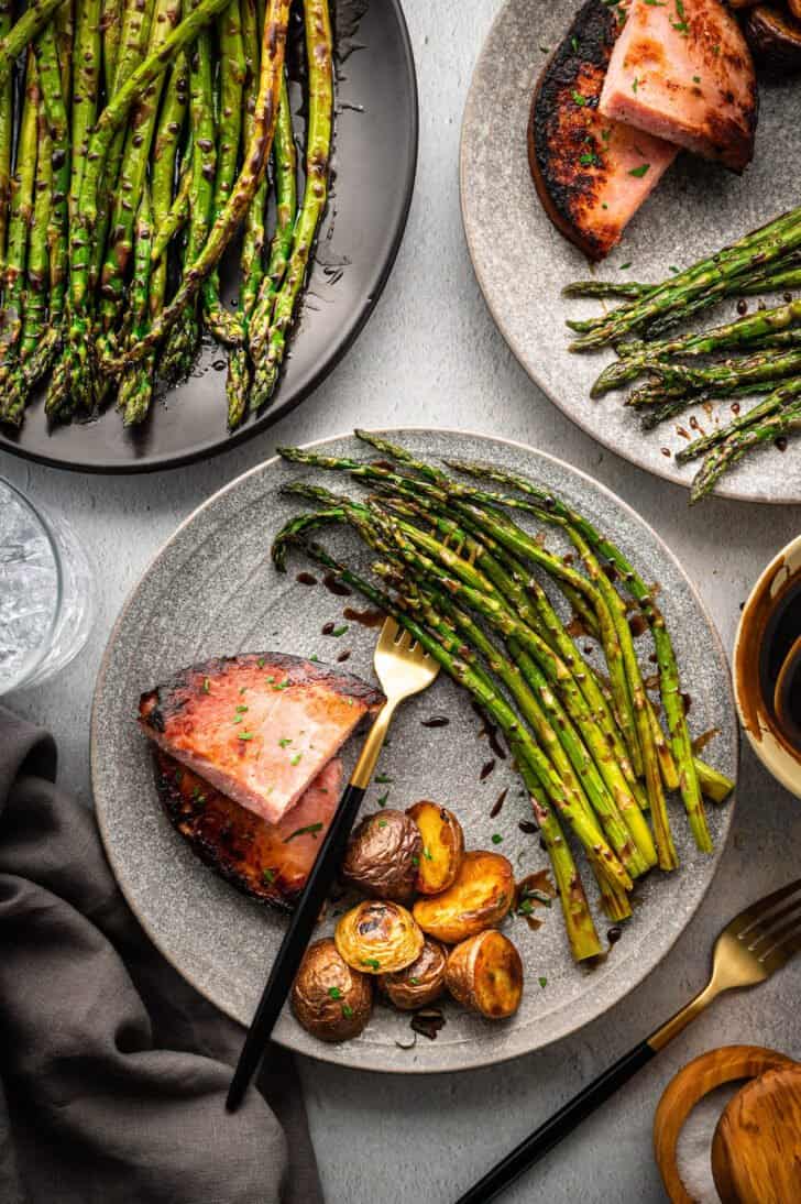Dinner plates filled with ham, roasted potatoes, and roasted asparagus with balsamic glaze.