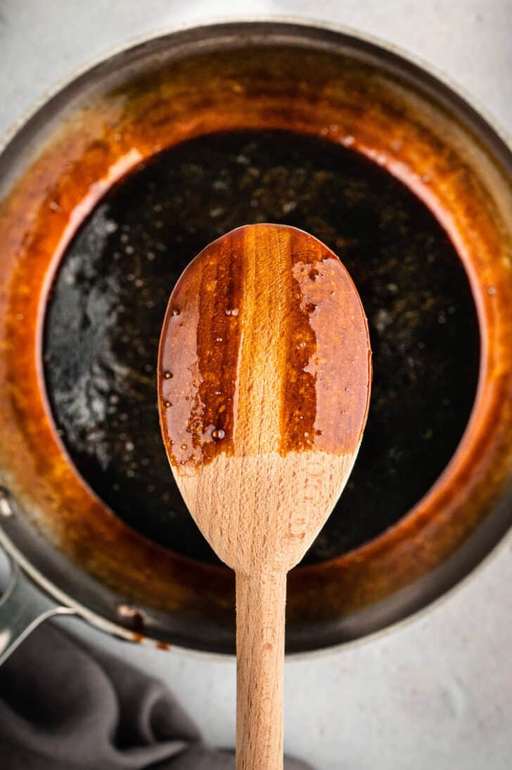 A wooden spoon coated in a vinegar reduction with a finger line in the coating, demonstrating how to make a balsamic glaze recipe. 