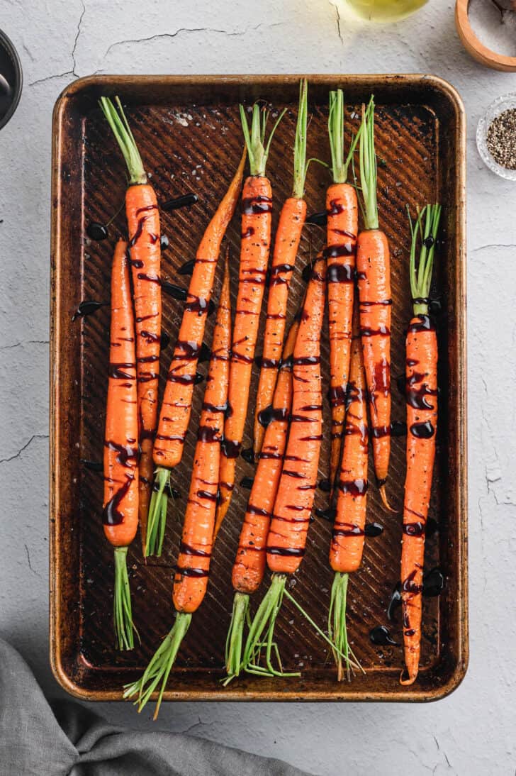 A textured baking pan filled with carrots with their tops on, drizzled with a dark glaze.