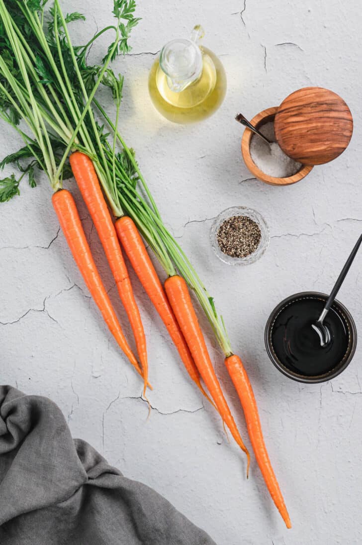 Ingredients laid out on a light surface, including carrots, dark vinegar, salt and pepper.