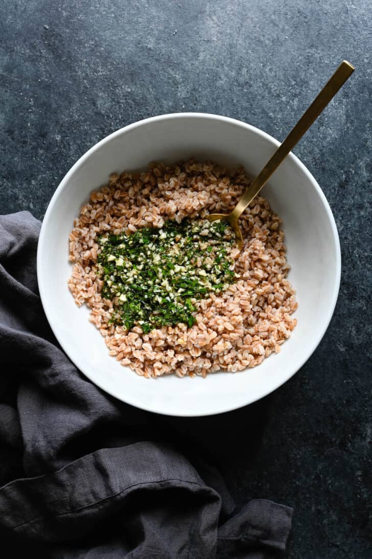 Cooked farro in a white bowl topped with an herb and garlic mixture.