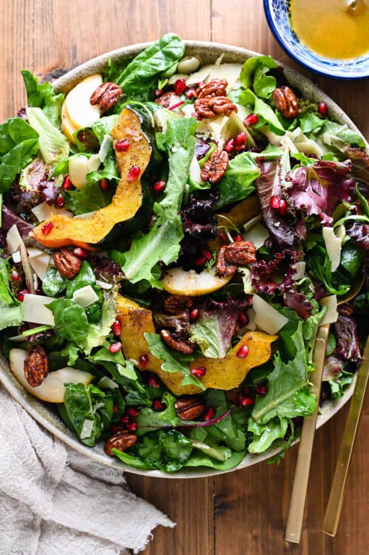 A large round platter filled with salad for Thanksgiving made with pears, pomegranate seeds, roasted acorn squash, candied pecans, Parmesan cheese and mixed greens.