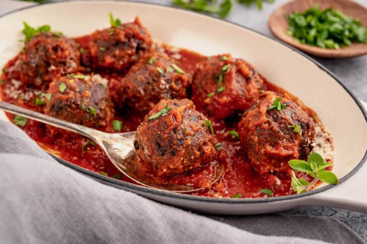Black bean meatballs smothered in marinara in a baking dish, with a spoon lifting out one bean ball.