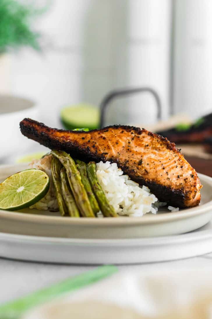A piece of blackened salmon on top of white rice and asparagus with a lime garnish.
