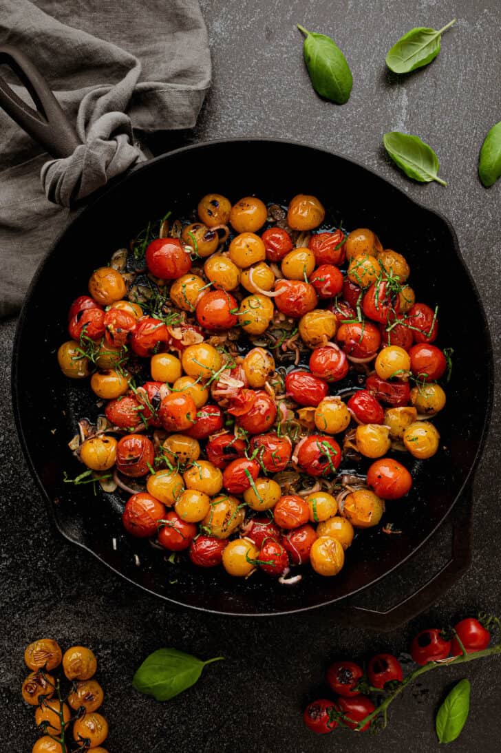 Large cast iron skillet filled with blistered tomatoes, shallots and basil.