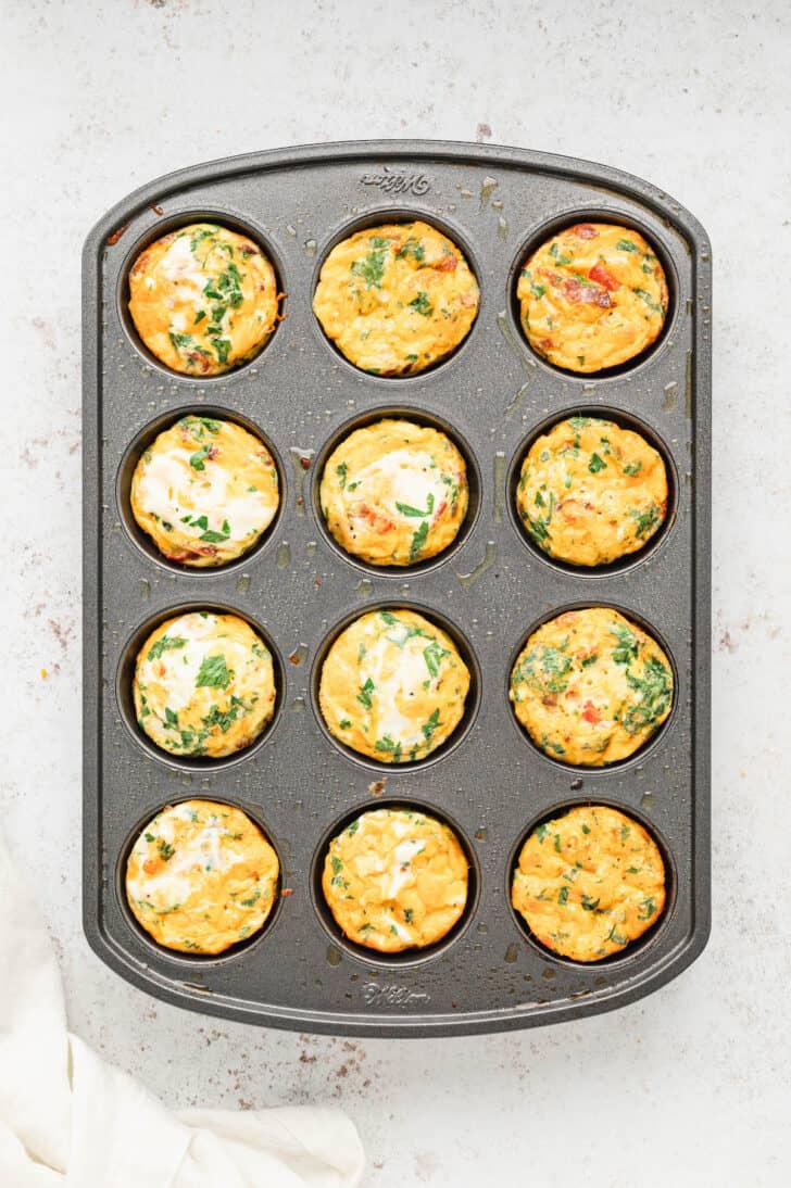 A 12-cup muffin pan filled with breakfast egg muffins made with bacon, cheese and veggies, fully baked.