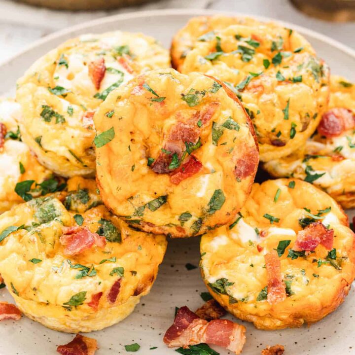 A white plate topped with breakfast muffins made with eggs, bacon, veggies, cheese and herbs.