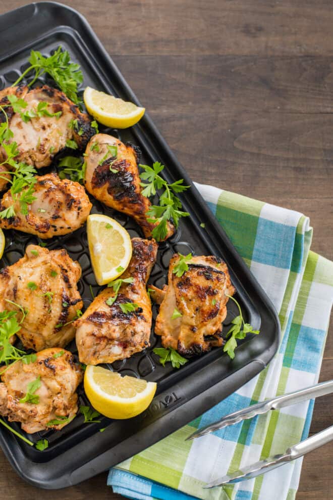 Black plastic tray of buttermilk marinated grilled chicken garnished with parsley and lemon.