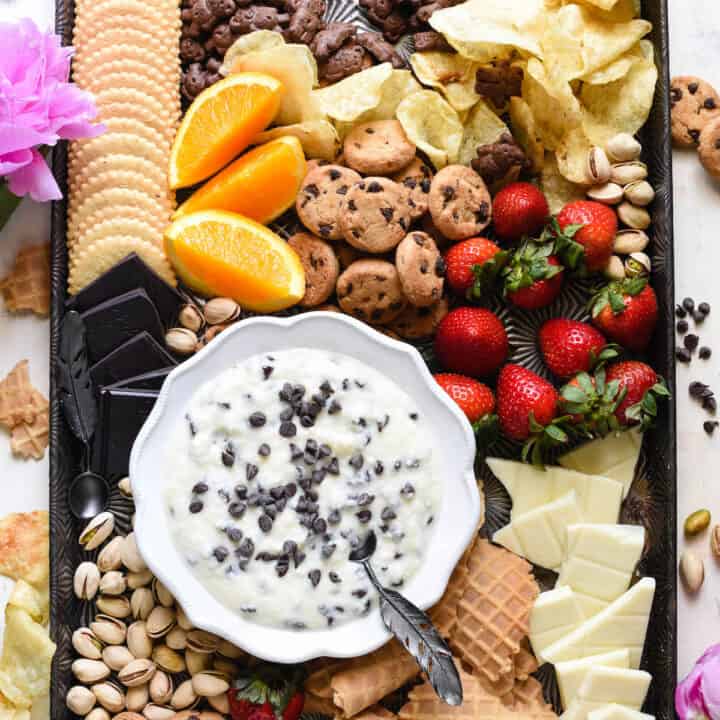 Overhead shot of large pan with bowl of dessert dip and cookies, fruit, nuts and potato chips for dipping.