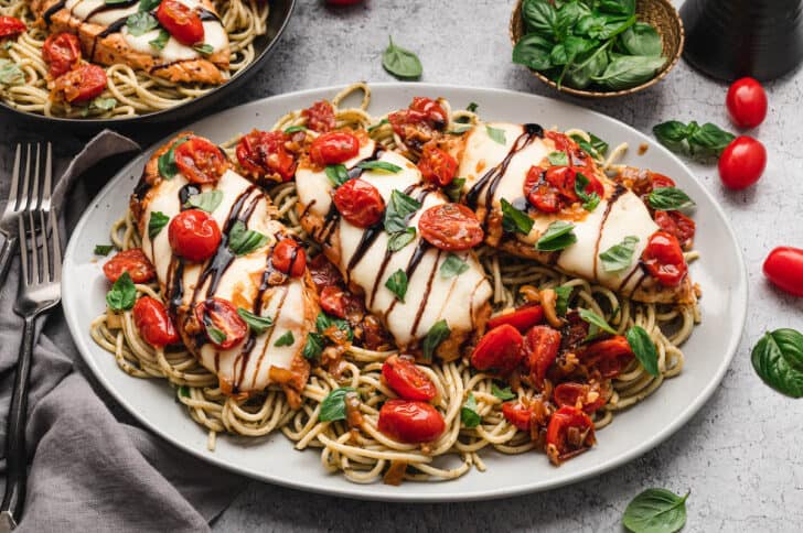 A white platter topped with baked caprese chicken over pesto spaghetti.