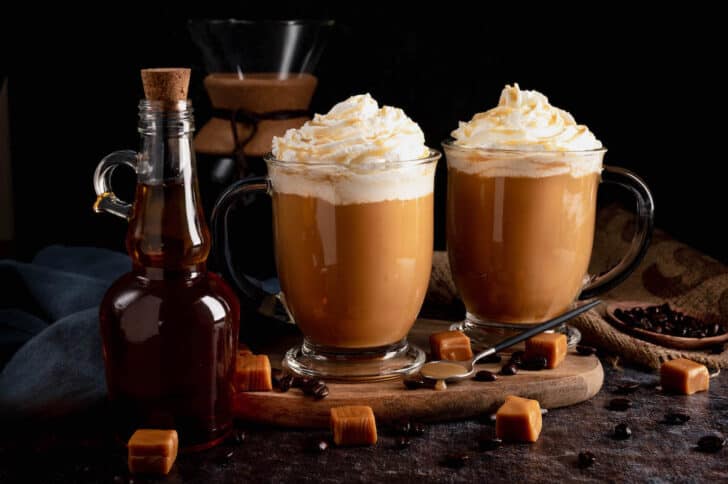 Two mugs of coffee with caramel sauce and whipped cream garnishes.