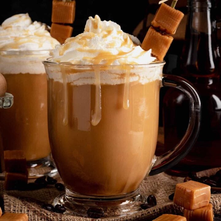A glass mug filled wth creamy caramel coffee and garnished with whipped cream and a skewer of caramel candies.