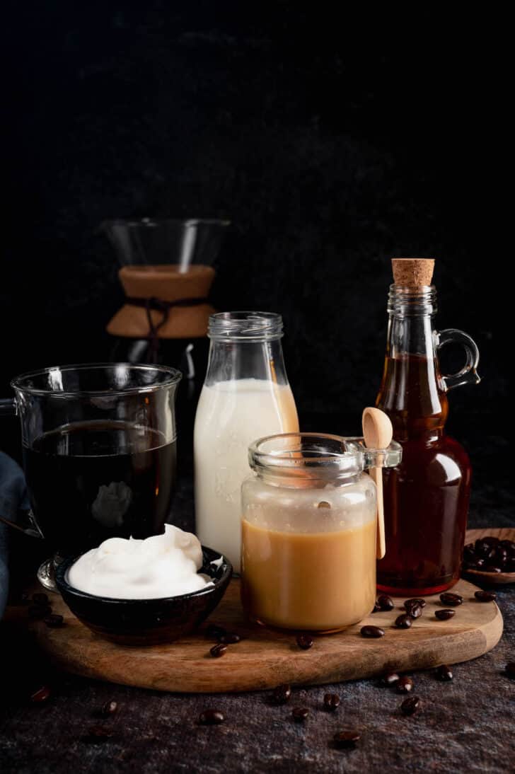 The ingredients needed to make a caramel coffee recipe, including milk, caramel sauce, caramel syrup, coffee and whipped cream.