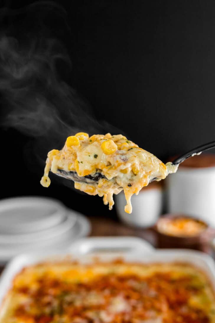 A spoonful of corn casserole with cheeese, steaming against a black background.