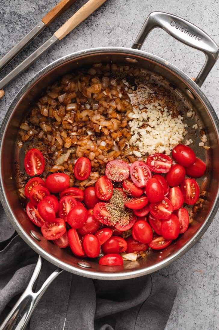 Halved grape tomatoes, cooked onions and minced garlic in a stainless steel skillet.