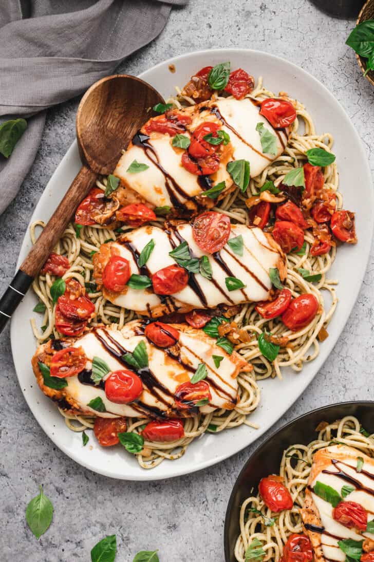 A white platter topped with chicken caprese bake over pesto spaghetti.