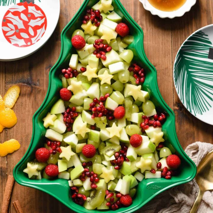 Christmas fruit salad made with grapes, raspberries, pomegranate seeds, kiwi, pineapple and green apple, arranged in a green Christmas tree shaped baking pan.