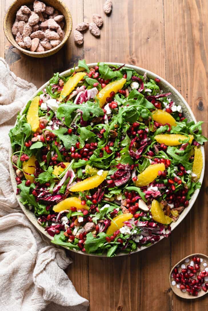 Holiday side dish made with greens, oranges, cheese, pomegranate seeds and nuts, arranged on a large round platter.