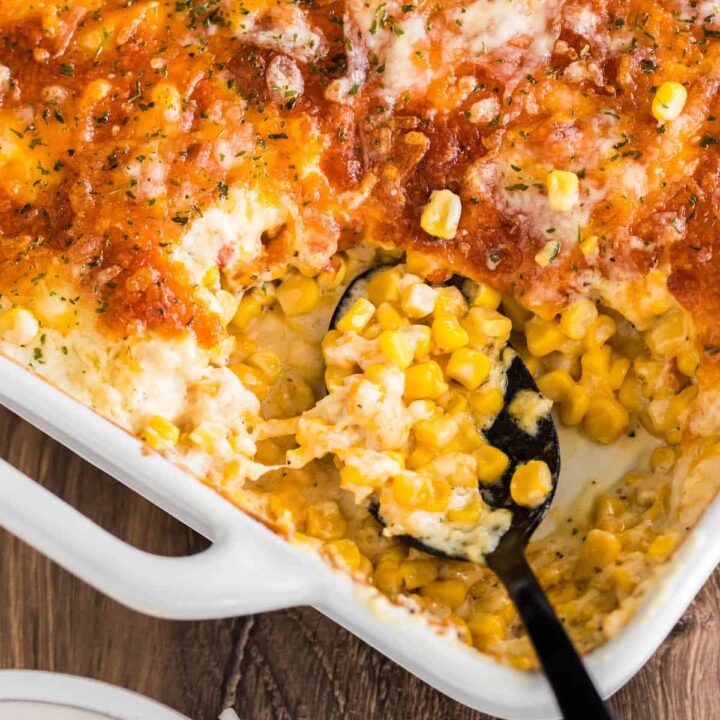 A white baking dish full of cheesy corn casserole with a black spoon taking a scoop out.