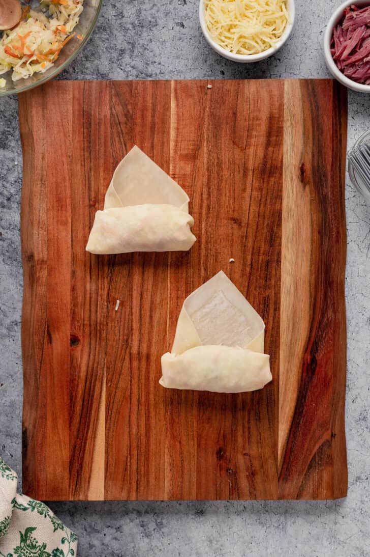 Small envelopes of egg roll wrappers on a wooden cutting board.