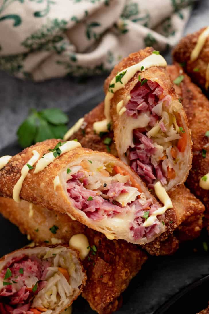 Halved reuben egg rolls drizzled in creamy sauce on a serving platter.