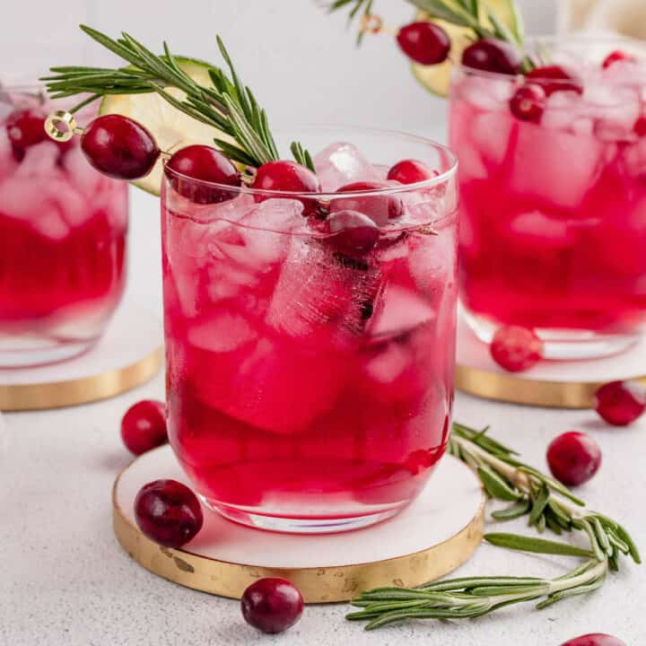 A cranberry rosemary cocktail garnished with a rosemary sprig, fresh cranberries and a wheel of lime.