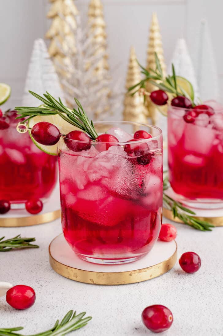 Three cranberry rosemary cocktails garnished with rosemary sprigs and fresh cranberries.