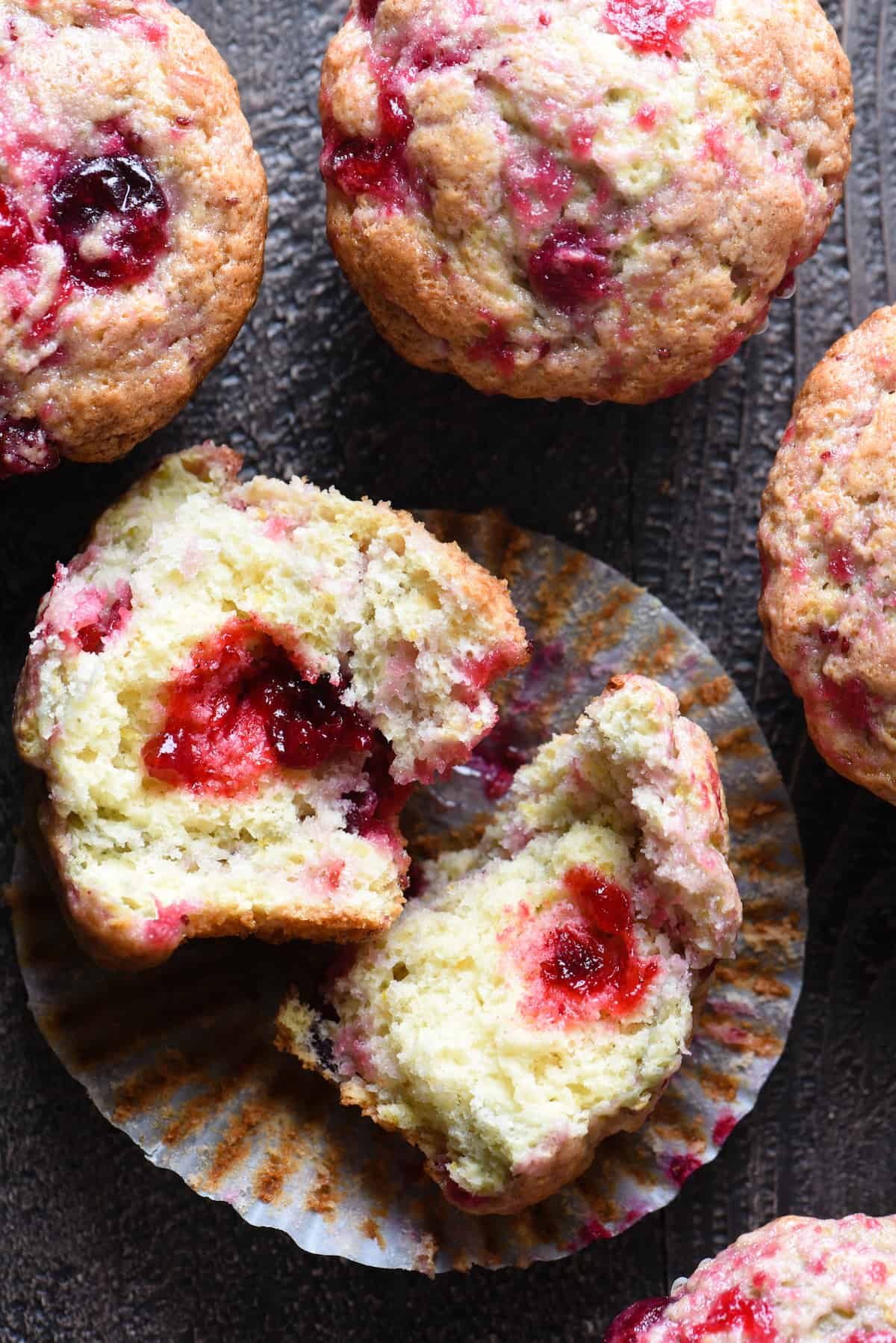 Overhead photo of cranberry muffins, with one broken in half to reveal inside.