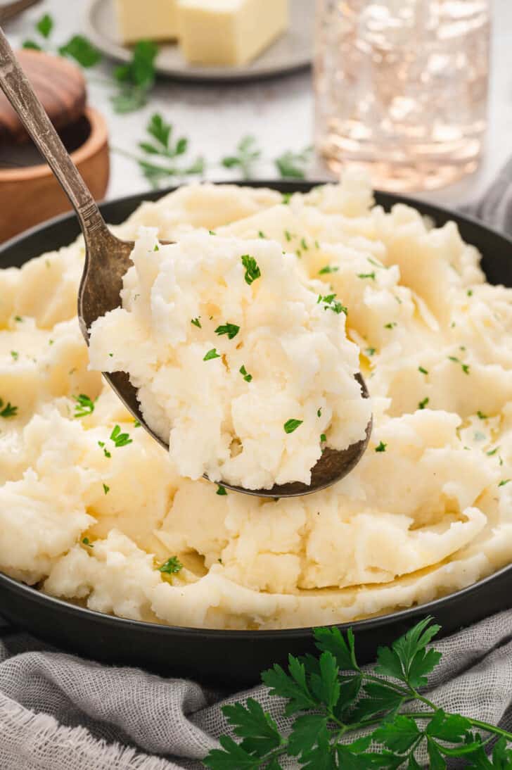 A bowl of a creamy mashed potatoes recipe with a spoon lifting some up.