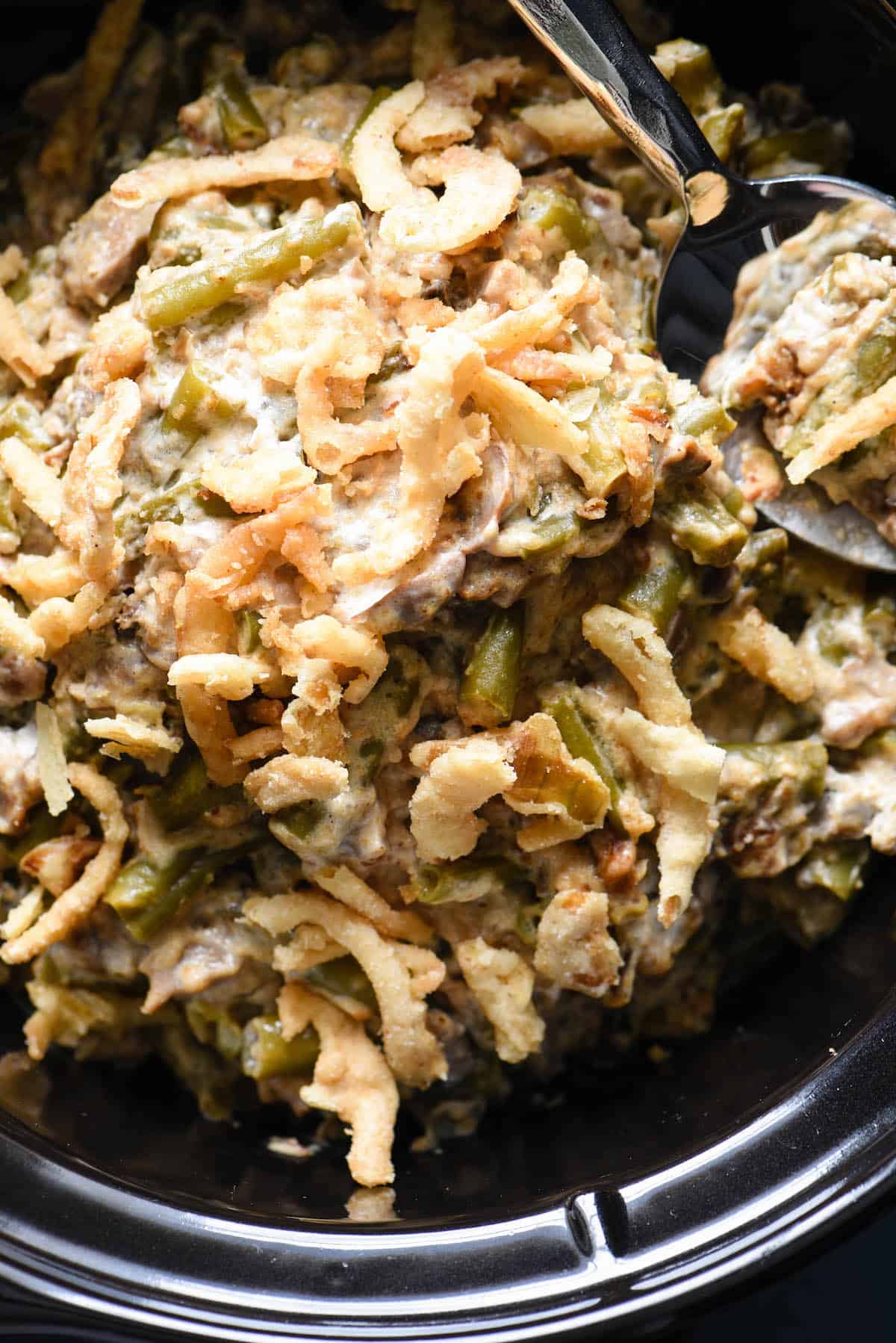 A crock pot green bean casserole with a spoon digging into it.