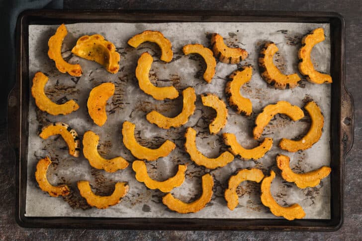 A baking pan topped with roasted half moon slices of a fall gourd.