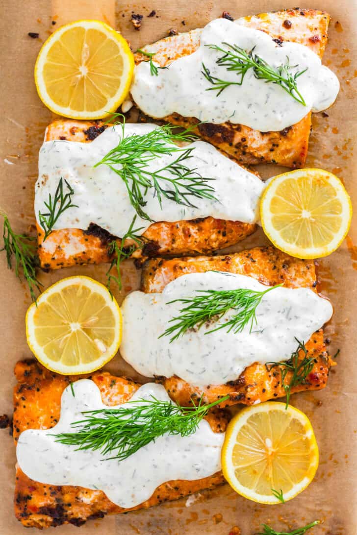 Dill sauce for salmon spread over cooked fish, with lemons and dill garnishing the fish.