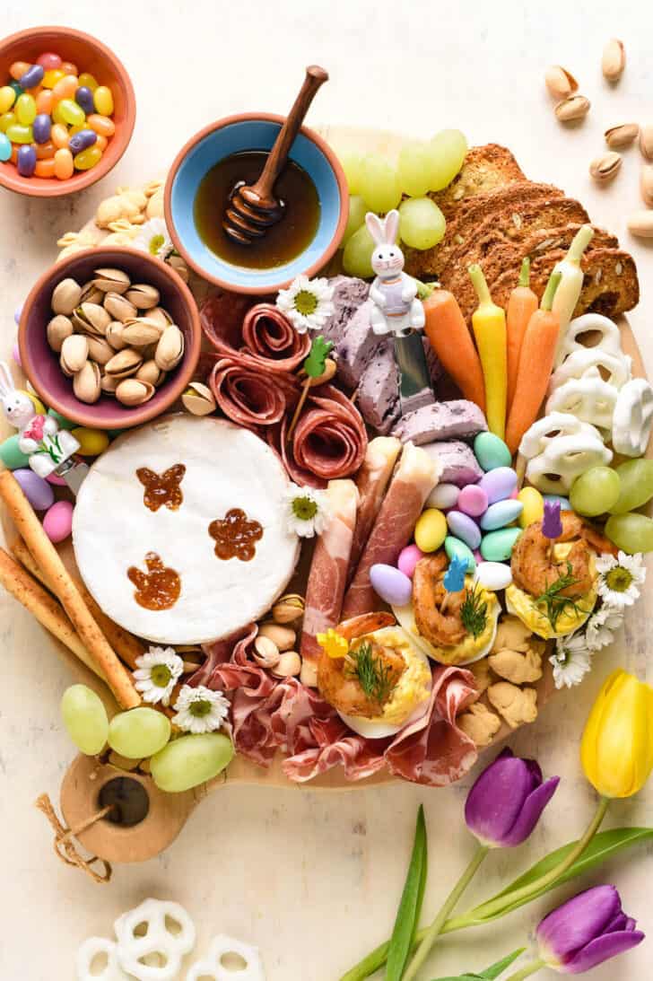 An Easter charcuterie board idea including cheese, meats, vegetables, candy, nuts, crackers, honey and deviled eggs.