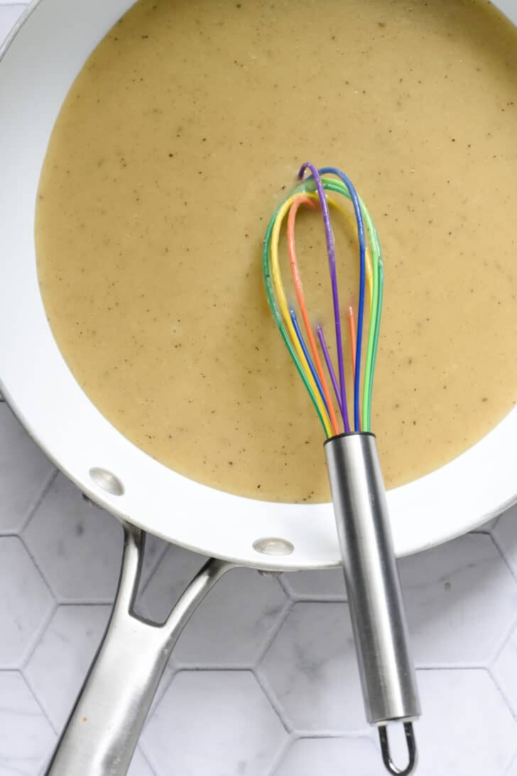 A white skillet filled with homemade gravy, with a multicolored whisk.