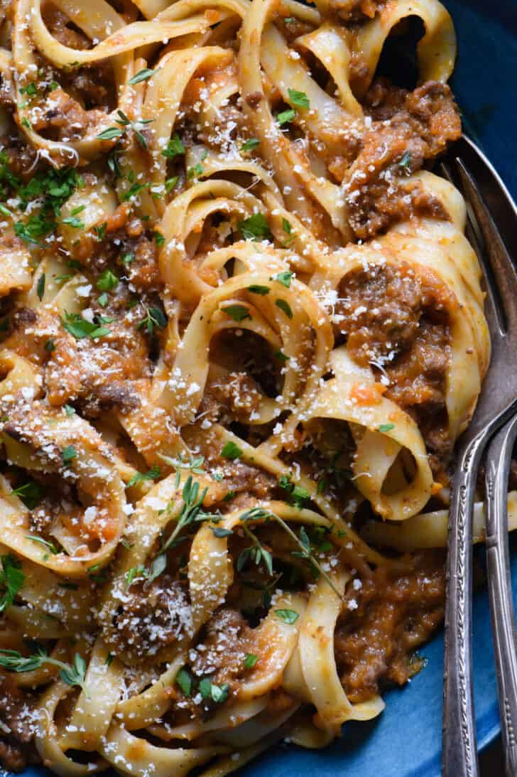 A closeup on pasta bolognese garnished with herbs and Parmesan cheese.