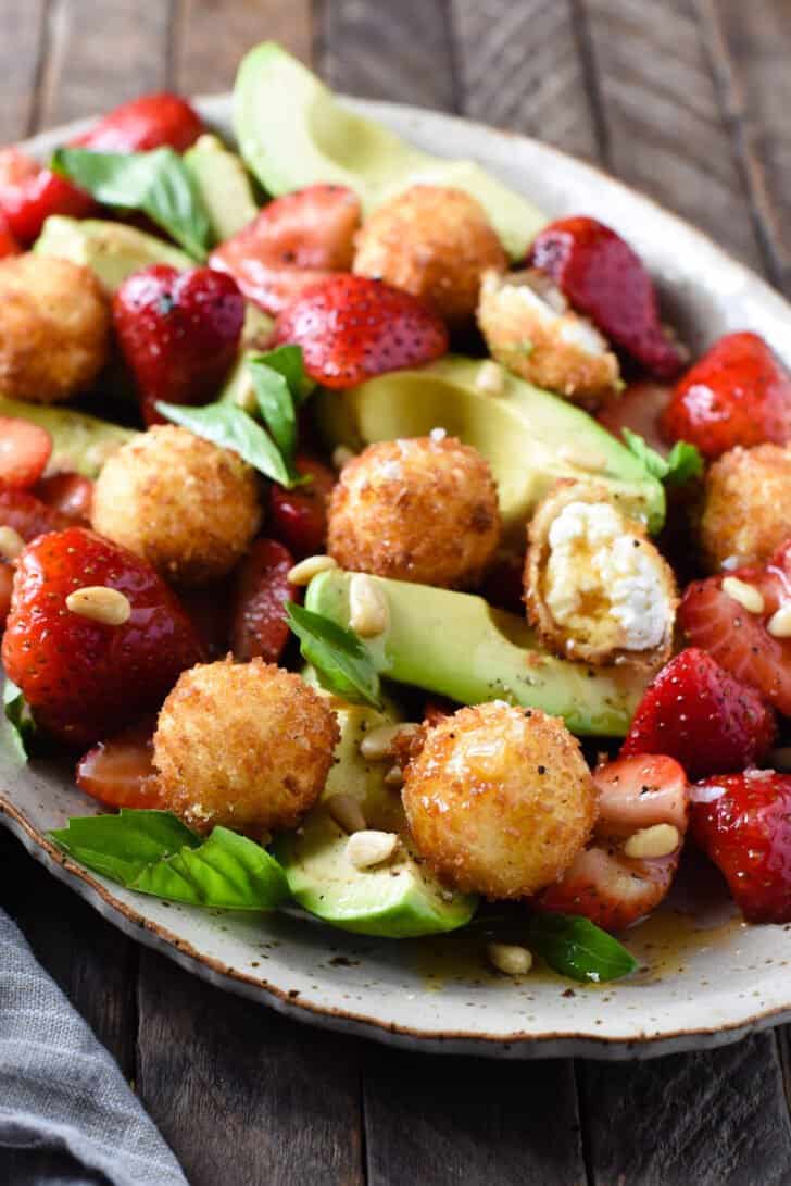 Strawberries, avocado, nuts and herbs with fried goat cheese fritters on a rustic speckled platter.