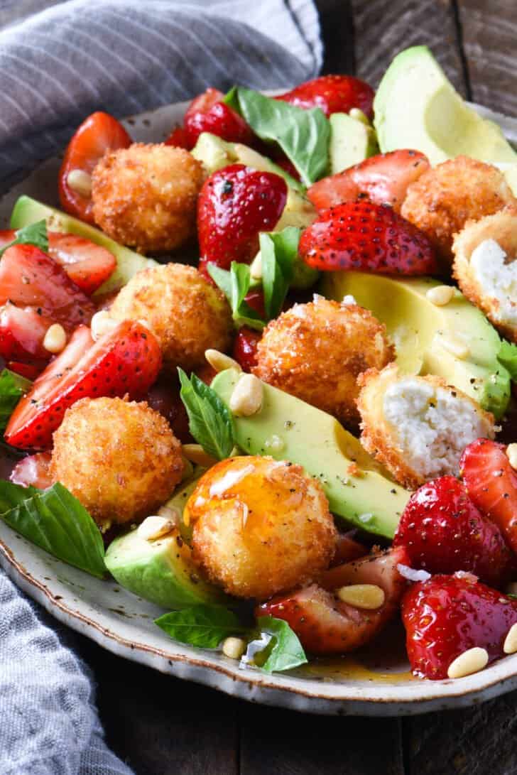 A large platter filled with fried goat cheese balls, strawberries, avocado, pine nuts and basil.