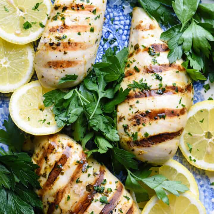 Grilled chicken breasts on blue platter with lemon slices and fresh parsley.