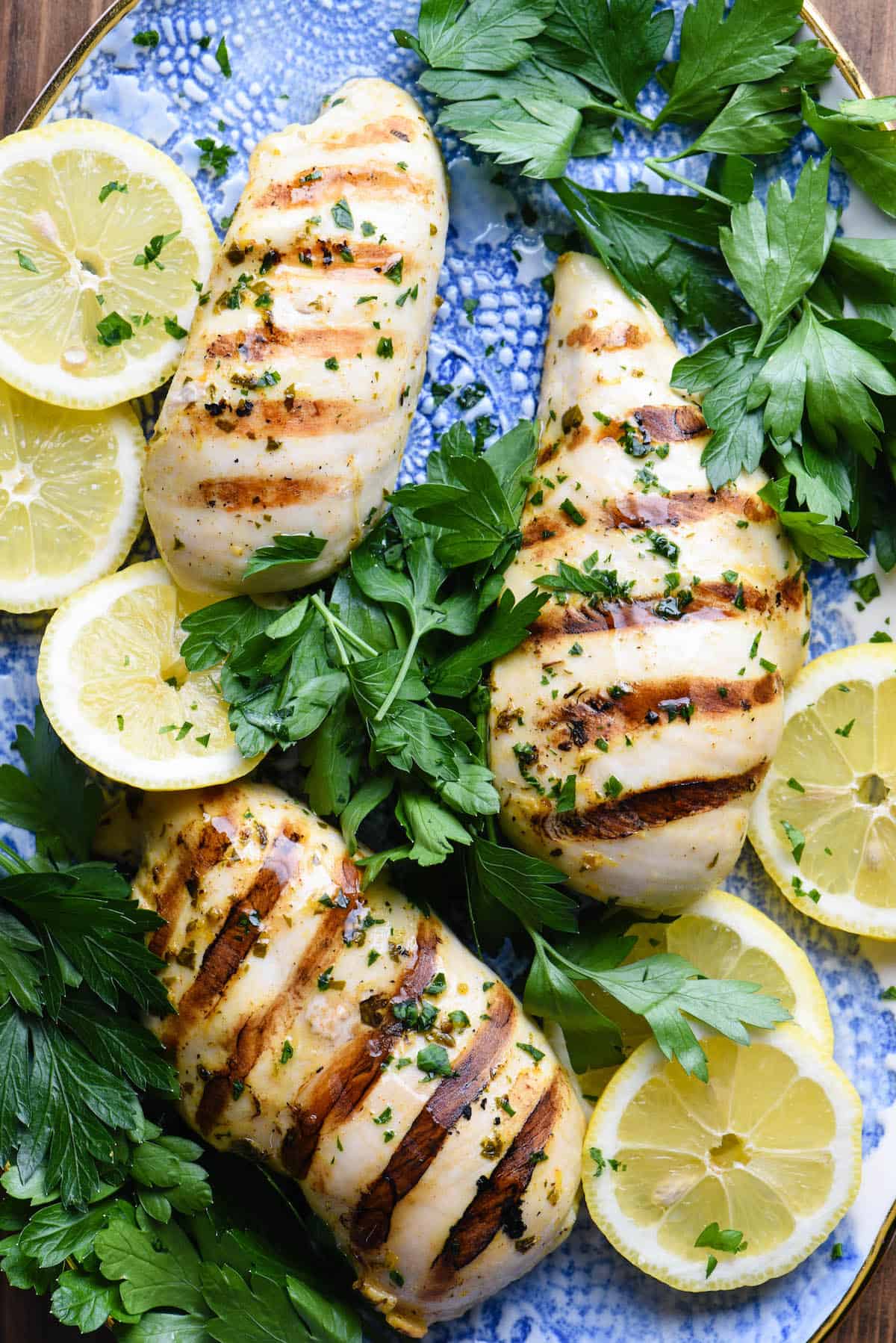 Cooked chicken pieces on pretty blue platter with herbs and lemons slices.