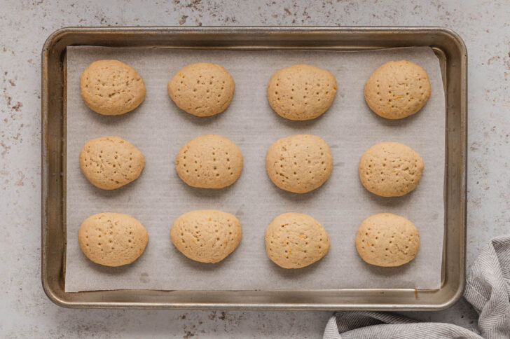 A rimmed baking pan lined with parchment paper, topped with oval-shaped cookies.
