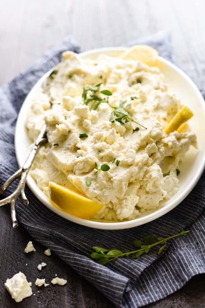 Creamy lemon spuds on white platter, garnished with herbs and lemon.