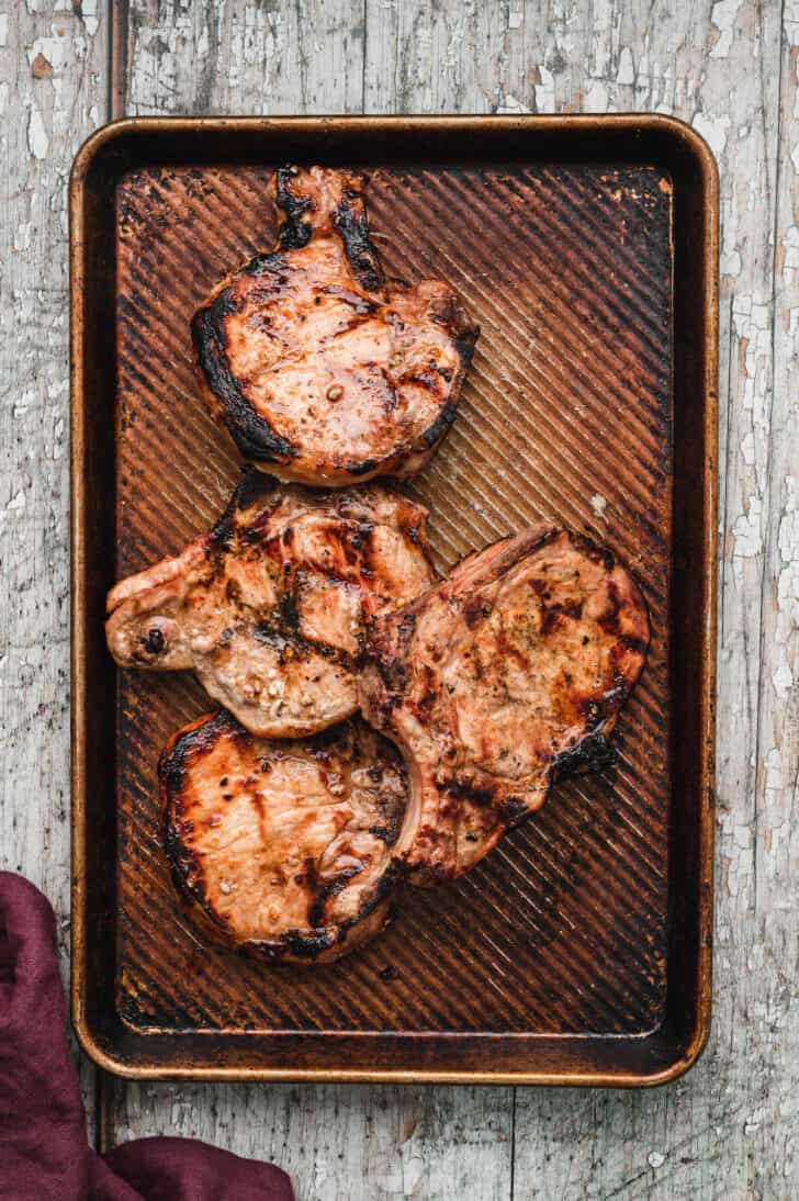 Four grilled pork chops on a textured baking pan.